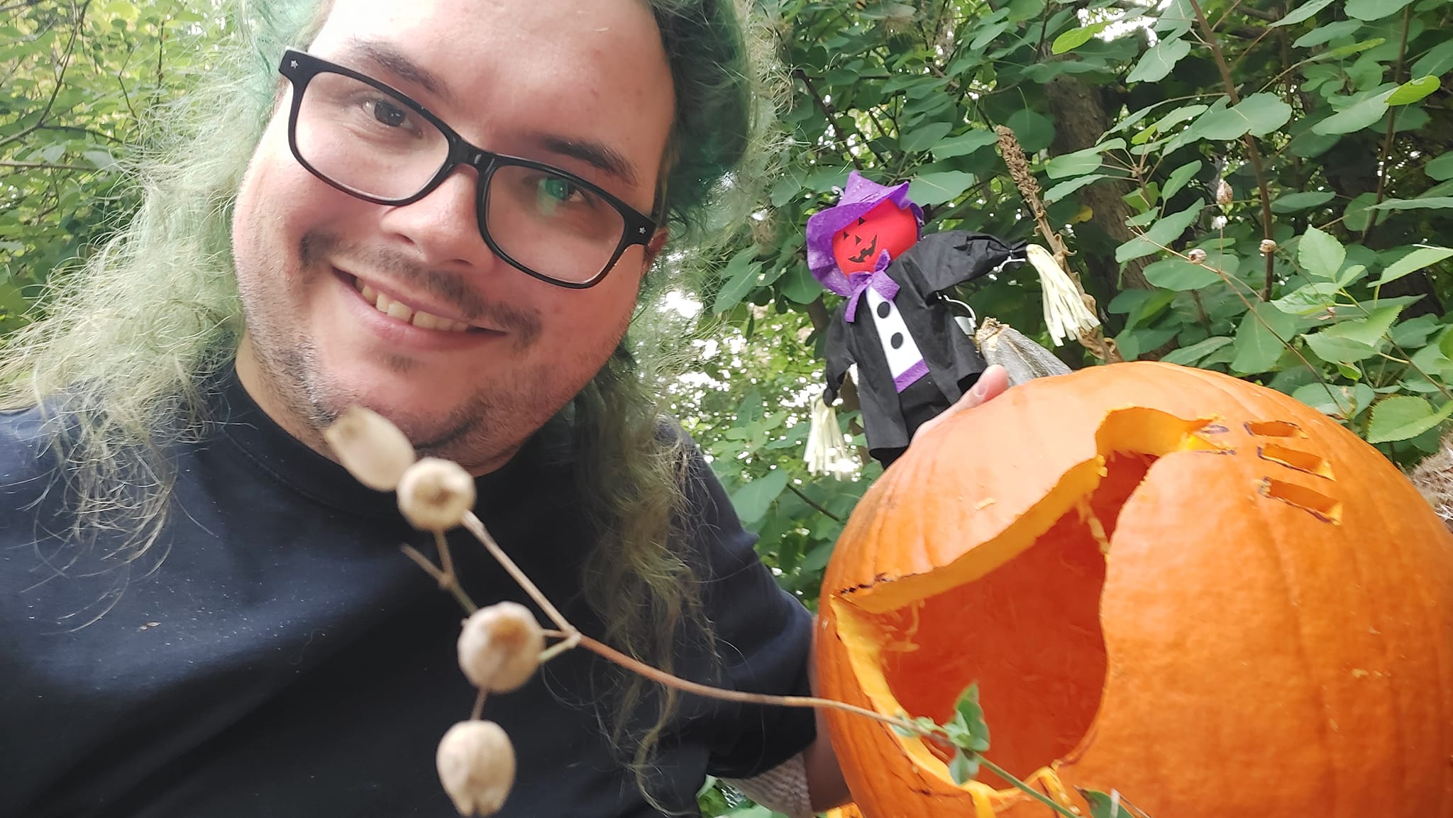 A man with long green hair and no beard holds large pumpkin with an Untitled Goose Game goose carved in it